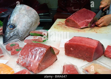 Frau schneidet ein Stück frischen Thunfisch mit großen Messer am Stall in La Boqueria-Markthalle in Barcelona, Spanien Stockfoto