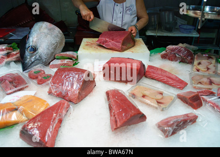 Frau schneidet ein Stück frischen Thunfisch mit großen Messer am Stall in La Boqueria-Markthalle in Barcelona, Spanien Stockfoto