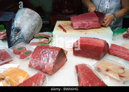 Frau schneidet ein Stück frischen Thunfisch mit großen Messer am Stall in La Boqueria-Markthalle in Barcelona, Spanien Stockfoto