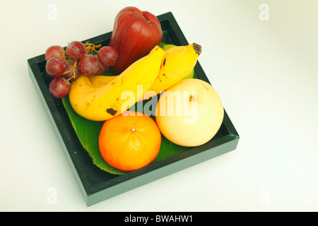 Exotische Südfrüchte (Banane, gelber Apfel, Wachs (Wasser, Rose) Apfel, Mandarine, eine Reihe von roten Trauben) in einer schwarzen quadratischen Platte. Stockfoto