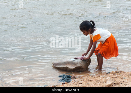 Junge indische Mädchen Wäsche mit der Hand auf einem Stein im Fluss. Andhra Pradesh, Indien Stockfoto