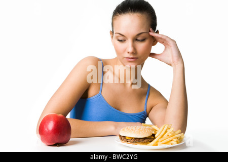 Porträt von hübschen jungen Mädchen entscheiden, was zu essen: einen Apfel oder Hamburger mit Pommes frites Stockfoto