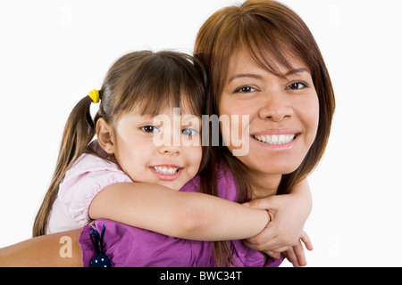 Nettes Kind umarmen ihre schöne Mutter und beide Blick in die Kamera mit einem Lächeln Stockfoto