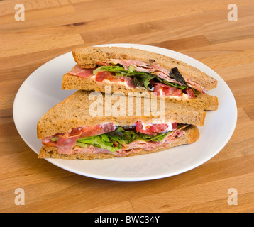 Essen, Mahlzeit, Snack, Speck-Salat und Tomate BLT dunkles Brot Sandwich auf einem weißen Teller auf einer hölzernen Tischplatte. Stockfoto