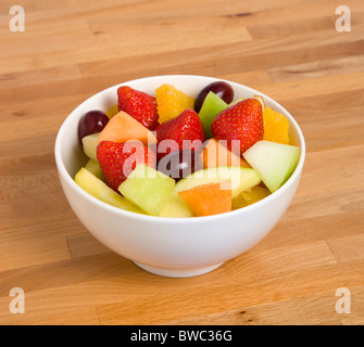 Lebensmittel, Obst, Salat, weiße Schüssel mit Salat von frischen Früchten auf einer hölzernen Tischplatte. Stockfoto