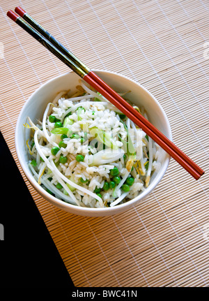 Essen, gekochte, Reis, gebratener Reis mit Gemüse in eine Schüssel geben mit Stäbchen auf einer Bambusmatte Tisch sitzen. Stockfoto