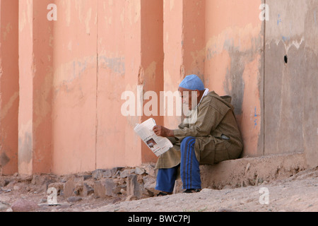 Ein marokkanische Mann sitzt und liest eine Zeitung im Schatten in der Stadt Ouarzazate, Marokko Stockfoto