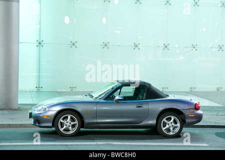 Mazda MX-5 Cabrio Sportwagen auf der Straße vor beleuchteten Glaswand in der Nacht Stockfoto