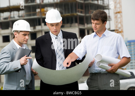 Porträt von drei Bauherren am Baustelle stehen und diskutieren neue Projekt von einer von ihnen gehaltenen Stockfoto