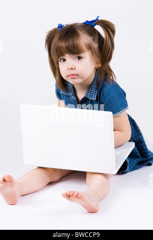 Neugierige Mädchen mit Laptop auf den Knien sitzen und Blick in die Kamera Stockfoto