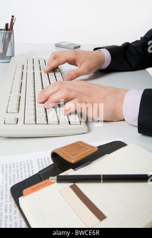 Nahaufnahme der männlichen Hände drücken Tasten mit Notebook und Unterlagen in der Nähe von Stockfoto