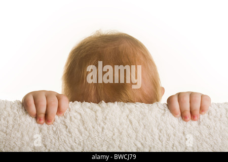 Entzückende Baby versteckt sein Gesicht hinter Schranke auf weißem Hintergrund Stockfoto