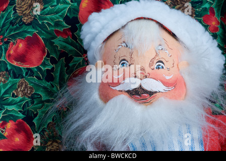 Lächelnder Weihnachtsmann aus der Nähe. Bemaltes Stoffgesicht mit Hut und Bart auf Apfel- und StechHintergrund. Stockfoto