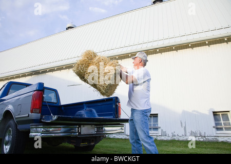 USA, Illinois, Metamora, Landwirt anhebende Heuballen auf Bauernhof Stockfoto