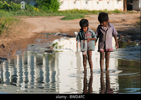 Glückliche junge indische Straße Jungs spielen in eine Wasserpfütze im Dorf Karnatakapalli Andhra Pradesh, Indien Stockfoto