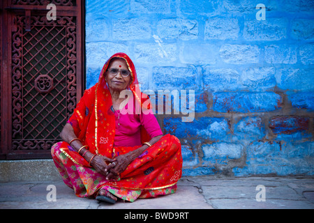 Alte Dame im roten Sari gegen die traditionellen blauen Architektur von Jodhpur. Stockfoto