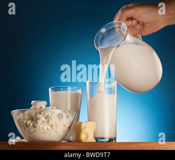 Mann Hand Gießen Milch aus Glas in das Glas. Isoliert auf einem blau. Stockfoto