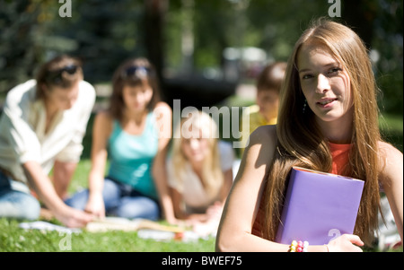 Porträt von fröhliches Mädchen mit Buch in Händen, Blick in die Kamera auf Grund ihrer Freunde Stockfoto