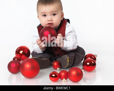 Sechs Monate altes Baby Junge sitzt mit einer roten Kugel Weihnachtsdekoration in seinen Händen. Isoliert auf weißem Hintergrund. Stockfoto