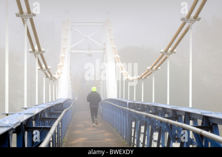 Nebligen Tag bei Teddington Lock, Westlondon, mit Jogger auf Brücke Stockfoto