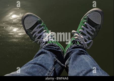 Beine mit Blue Jeans und grüne Converse Sneaker sitzt über dem Wasser Stockfoto