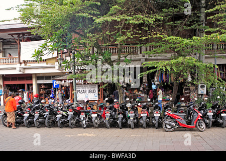 Motorräder und Roller parkten in einer Linie außerhalb der Ubud-Märkte. Bali, Indonesien. Eine Parkplatz-Inspektor ist auf der linken Seite. Stockfoto
