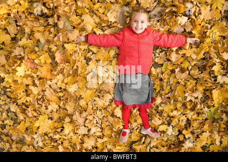 Glückliches Mädchen liegend auf Teppich trocken Ahornblätter und lachen Stockfoto