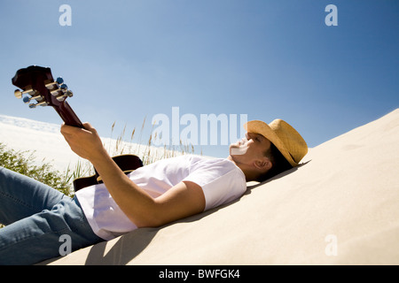 Bild von glücklichen Menschen in Cowboy-Hut, Gitarre zu spielen, während Sie sich am Sandstrand entspannen Stockfoto