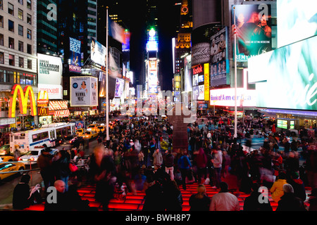 USA New York NYC Manhattan Menschen sitzen auf beleuchteten roten Stufen oder nachts auf dem Times Square an der Kreuzung 7th Avenue Stockfoto