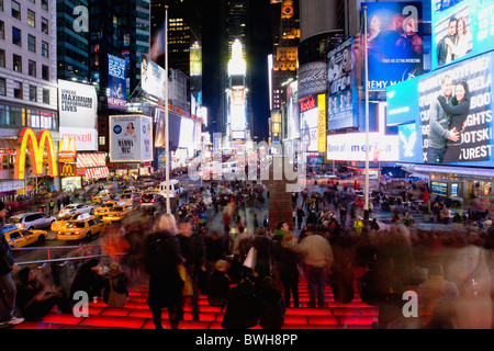 USA New York NYC Manhattan Menschen sitzen auf beleuchteten roten Stufen oder nachts auf dem Times Square an der Kreuzung 7th Avenue Stockfoto