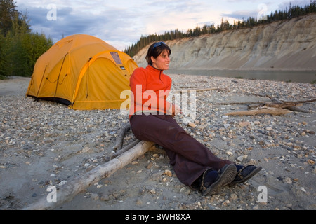 Junge Frau sitzend, genießen die Aussicht, entspannend, Zelt, hoch geschnittene Bank, Fluss Klippe, Erosion, hinten, oben Liard River Stockfoto