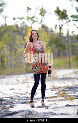 Attraktive junge Brünette Frau tragen helle Farbe Minikleid steht Holding Wein Flasche in das australische Outback-Land Stockfoto