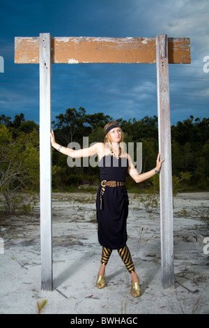 Attraktive junge Frau, die einem Nachlassen entworfen schwarz und gold Kleid mit gestreiften Strumpfhosen steht unter alten Holz-Zeichen Stockfoto