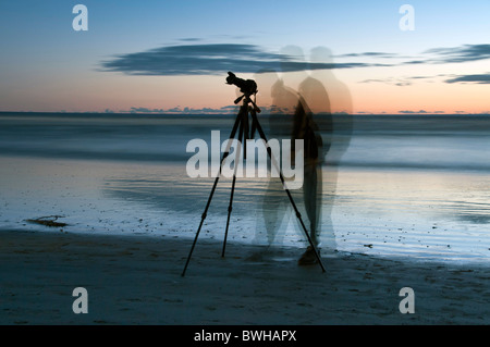 Ein Fotograf mit einem Stativ an der Ozeanküste ist mehrere Male während einer Langzeitbelichtung verwischt. Stockfoto