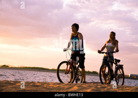 Figuren der glückliche Paar stehend am Meeresstrand mit ihren Fahrrädern und Sonnenuntergang Stockfoto