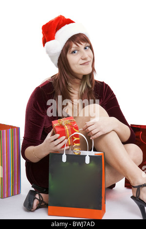 Das Mädchen in eine Weihnachts-Mütze sitzt unter Pakete mit Einkäufen Stockfoto