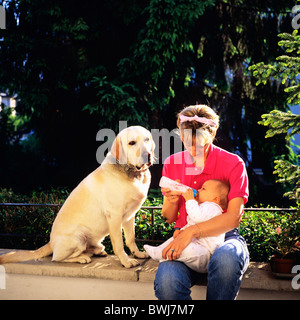 HERR JUNGE MUTTER MIT DER FLASCHE FÜTTERN IHR BABY UND LABRADOR GOLDEN RETRIEVER HUND Stockfoto