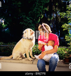 HERR JUNGE MUTTER MIT DER FLASCHE FÜTTERN IHR BABY UND LABRADOR GOLDEN RETRIEVER HUND Stockfoto