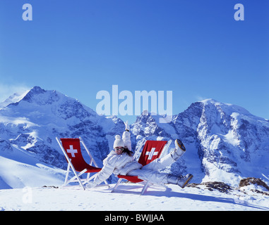 Frau Mütze Hut Winter Jacke Spaß Witz Freude Winter Liegestuhl nehmen es einfach entspannen Schweizer Kreuz Sonnen Berg Stockfoto