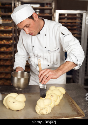 Baker Bürsten Ei Eigelb Verglasung auf rohe geflochten süßes Brot Stockfoto