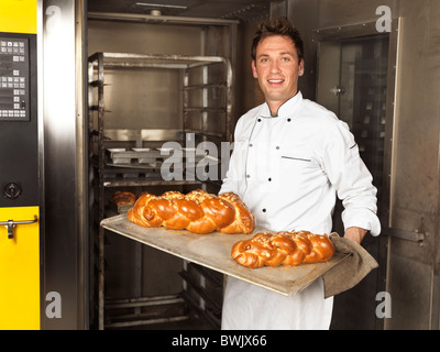 Porträt eines Bäckers hält ein Tablett mit frisch gebackenen süßen geflochtene Brot direkt aus dem Ofen Stockfoto