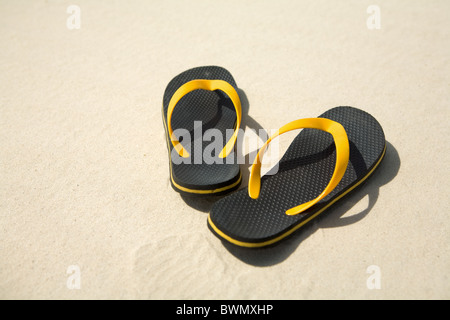 Bild von paar gelbe und schwarze Flipflops am Sandstrand Stockfoto