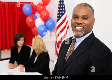 Porträt des Mannes in polling Ort, US-Flagge, Luftballons und Abstimmungen stand im Hintergrund, Metamora, Illinois, USA Stockfoto