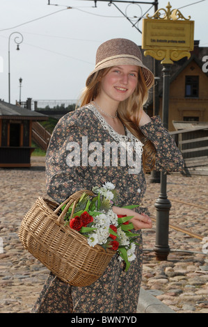 Mädchen in Homosexuell Kleid und Hut mit Korb mit Blumen in den Händen im alten Stil. Stockfoto