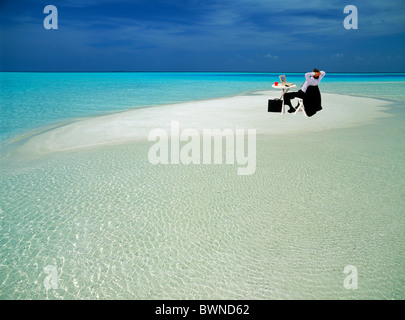 Geschäftsmann im Anzug mit Aktentasche sitzt im Stuhl am Tisch mit Laptop und Kaffee Tasse auf abgelegenen Sandbank in reine Einsamkeit Stockfoto
