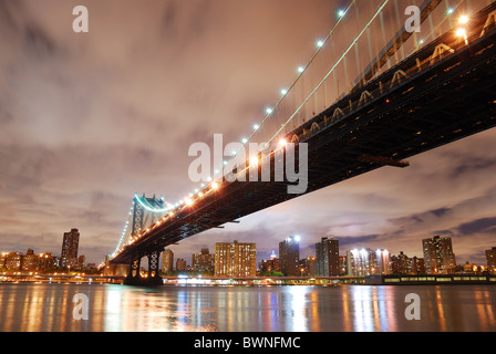New York City Manhattan Bridge mit Skyline der Stadt in der Nacht beleuchtet über Hudson River. Stockfoto
