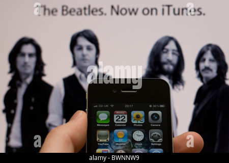 Ein Apple iPhone 4 mit der Apple-Website im Hintergrund zeigt die Beatles, jetzt erhältlich auf iTunes Stockfoto