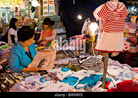 Frau Standbesitzer Zeitung lesen und Verkauf von Bekleidung in Namdaemun-Markt in Seoul in Südkorea in der Abenddämmerung. JMH3858 Stockfoto