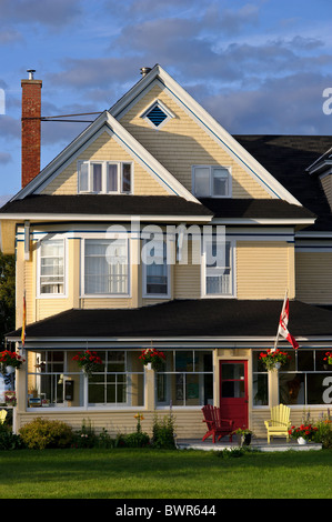 Bed And Breakfast in New Brunswick Baie de Chaleur gelbe Haus gelb Adirondack Stuhl erreichte Dach Sonnenuntergang kanadische Flagge Stockfoto