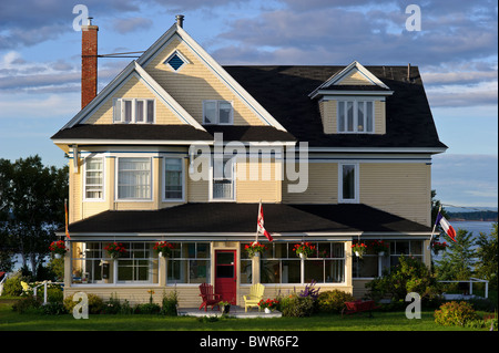 Bed And Breakfast in New Brunswick Baie de Chaleur gelbe Haus gelb Adirondack Stuhl erreichte Dach Sonnenuntergang kanadische Flagge Stockfoto